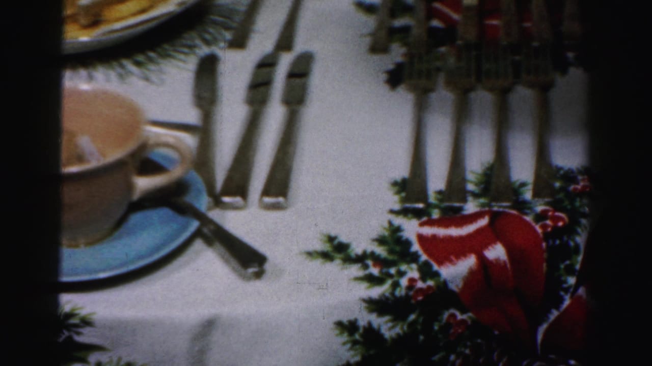 Albany 1956 home-movie frame showing a holiday table with a teacup, blue saucer, silverware, crackers, cheese, and festive cloth.