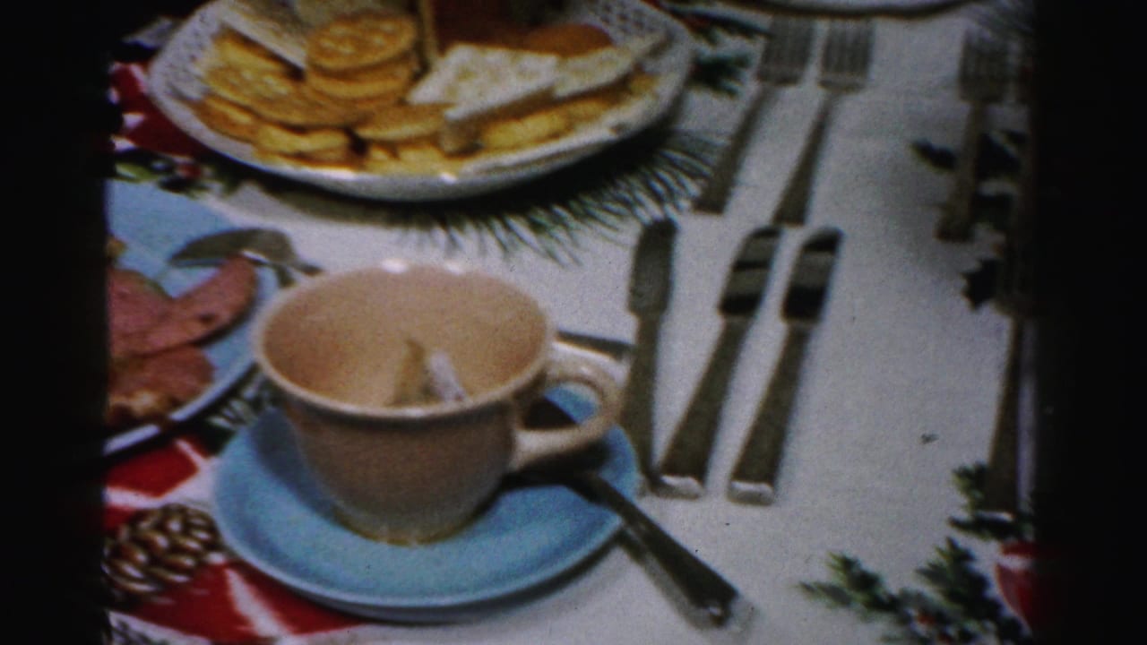 Teacup on blue saucer beside silverware, crackers, cheese, and holiday table decorations.