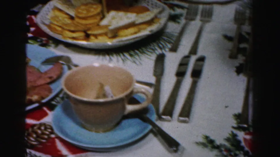 Albany 1956 holiday table frame with a teacup on a blue saucer, silverware, crackers, cheese, and red ribbon tablecloth detail.
