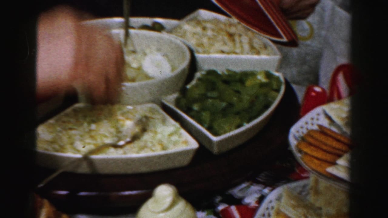Hand reaches toward a white serving bowl on a crowded holiday table.