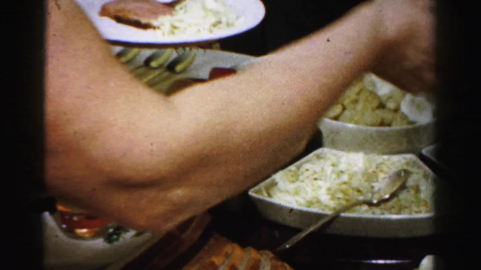 A person's arm and plate appear over a 1950s Albany Thanksgiving table with serving bowls, green vegetables, bread, and a spooned dish.