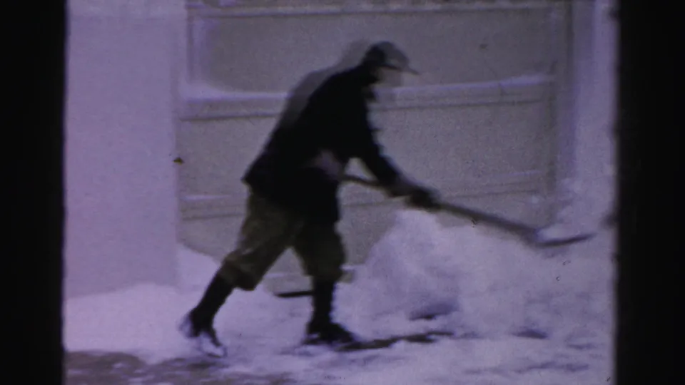 The man appears in motion, pushing or lifting snow with a shovel in front of a garage in Albany winter footage.