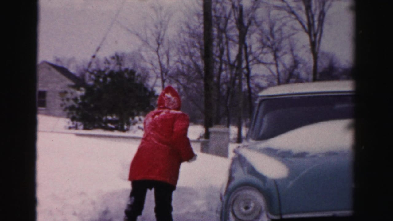 A woman in a bright red winter coat works with a shovel near a pale blue car on a snowy residential street in Albany, New York.