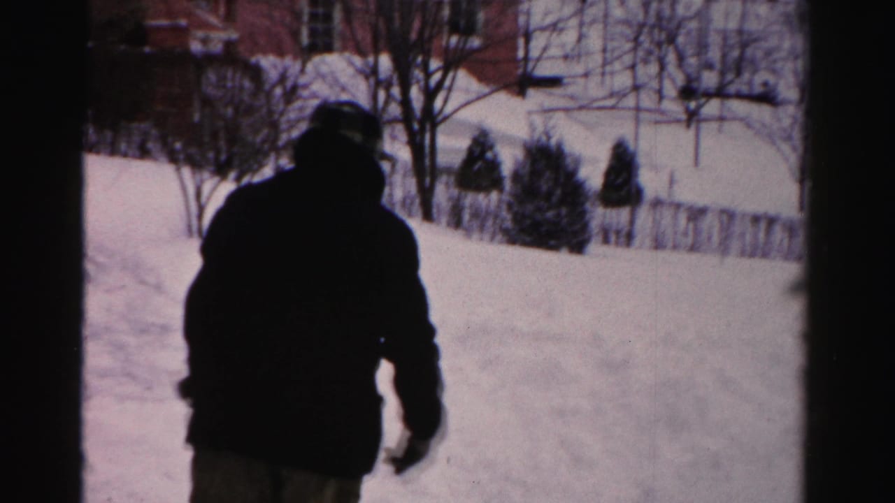 Dark-coated person walking through deep snow in a residential yard.
