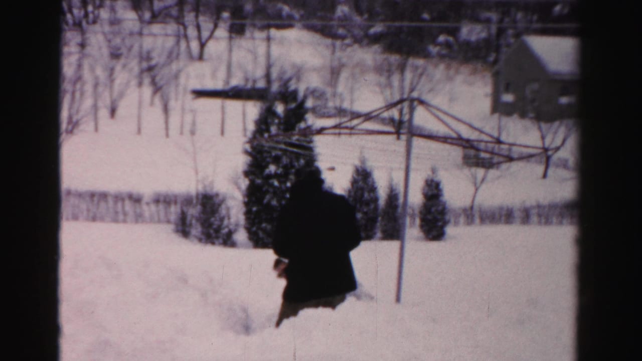 Adult in a dark coat moving away through snow with a clothesline and small building behind.