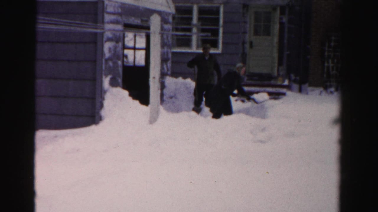 Two men in dark coats work through heavy snow near the entrance of an Albany home in 1956 8mm footage.