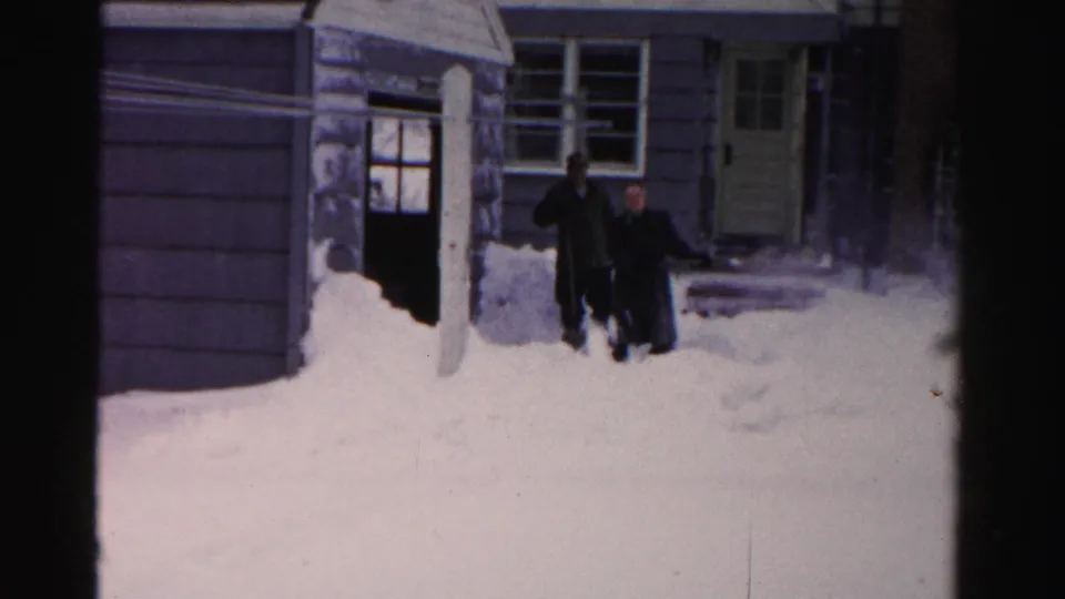 Two men continue clearing snow outside a residential doorway in Albany, New York, in supplied 1956 home-movie footage.
