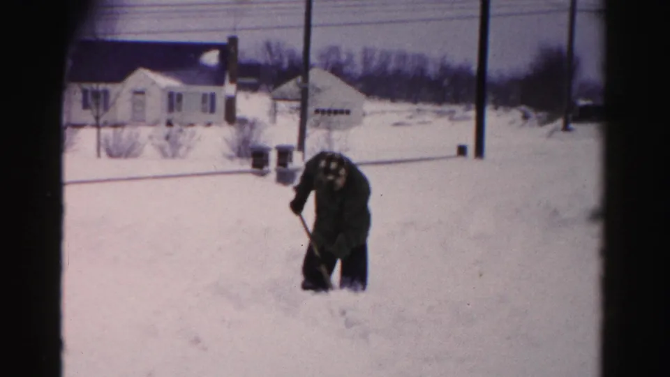 Man pausing while shoveling snow in a residential yard, Albany, New York area, circa mid-1950s, 8mm color film.