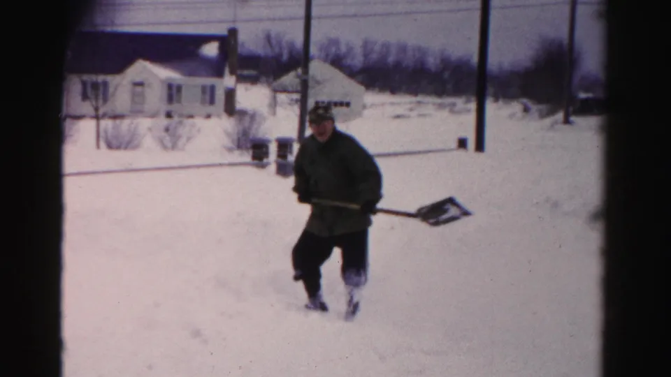 Man carrying snow shovel through deep snow in a suburban yard, Albany, New York area, circa mid-1950s, 8mm color film.