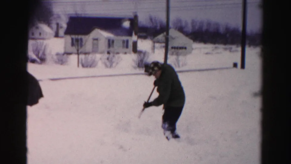 Man leaning on snow shovel in a residential yard, Albany, New York area, circa mid-1950s, on 8mm color film.