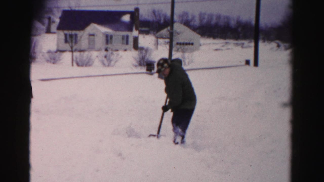 A man shovels snow in what appears to be a mid-1950s Albany, New York residential neighborhood, captured on 8mm home-movie film.