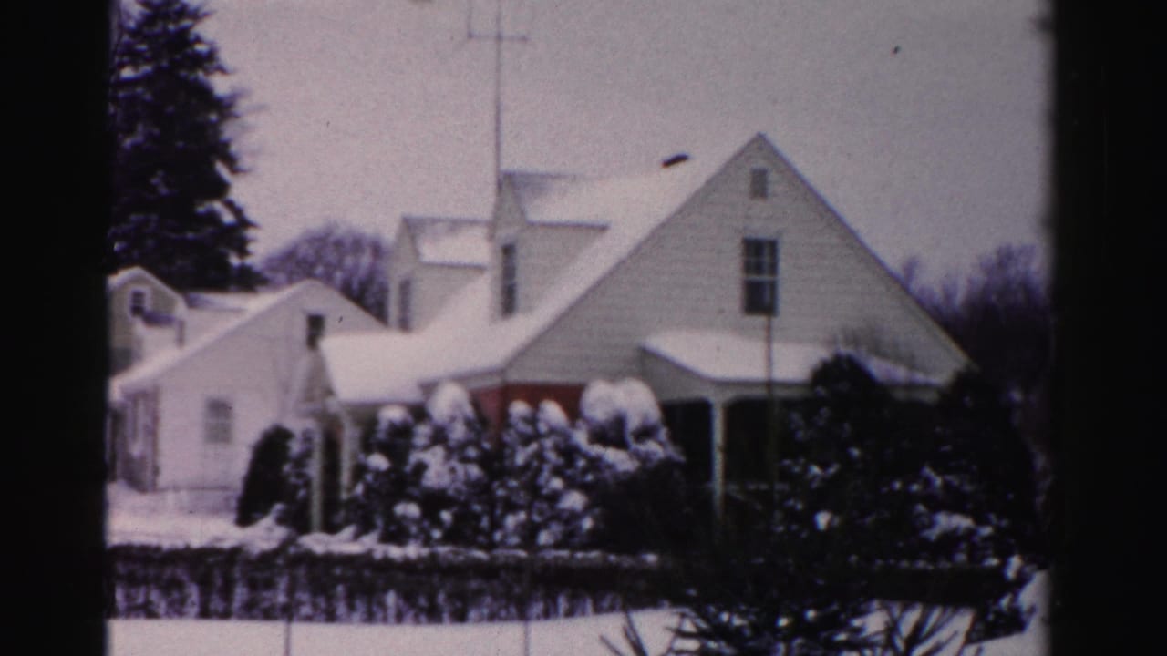 Snow-covered mid-century clapboard houses with TV rooftop antenna and snow-laden evergreen shrubs; Albany, New York area, circa mid-1950s winter, 8mm color film.