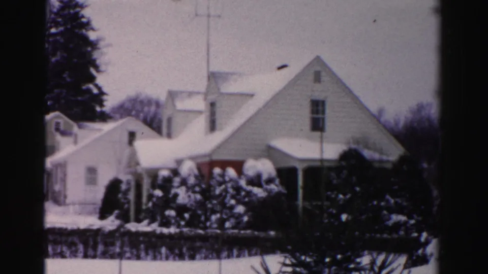 Snow-covered mid-century clapboard houses with TV rooftop antenna and snow-laden evergreen shrubs; Albany, New York area, circa mid-1950s winter, 8mm color film.