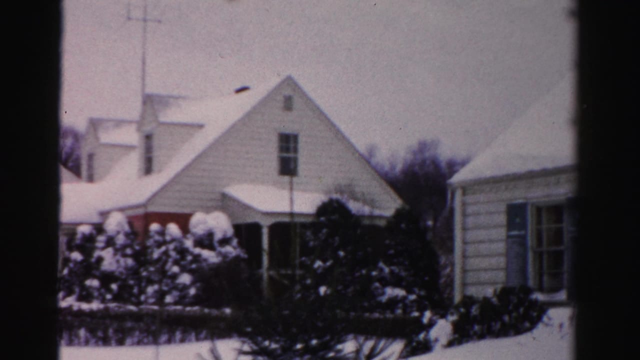 Continued view of snow-covered clapboard houses with rooftop TV antenna and shrubs; Albany, New York area, circa mid-1950s, 8mm color film.
