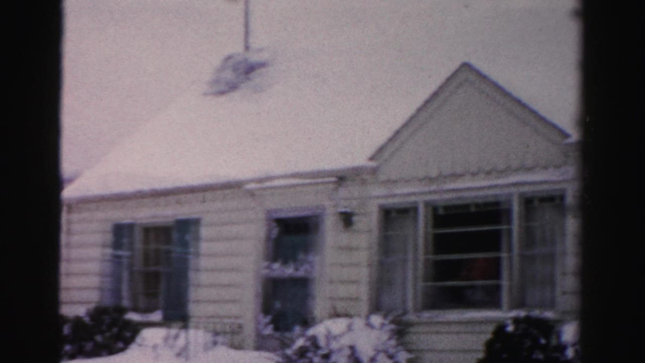 Snow-covered clapboard house exterior, left section with triangular gable at top, deep snow on ground and roof.