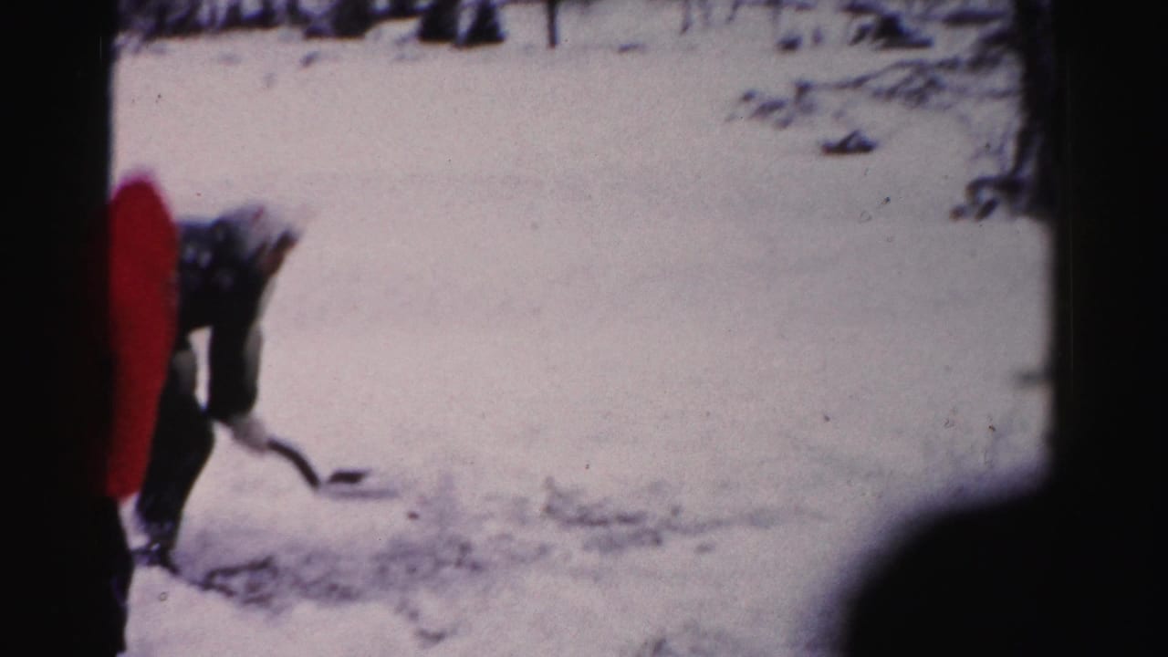 Two adults in winter outerwear playing in snow in a residential yard, consistent with mid-1950s Albany, New York 8mm home movie.