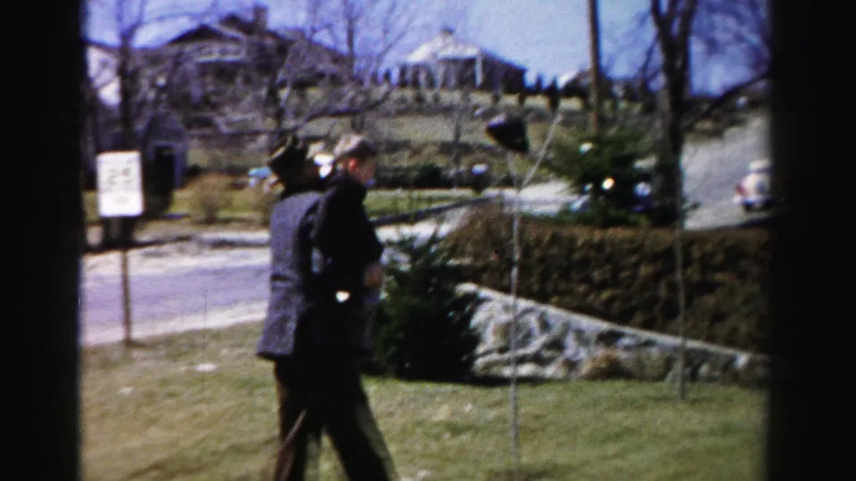 Man and child stand together on a suburban lawn in what appears to be mid-1950s Albany, New York; a two-story house with a prominent roofline and period automobiles visible behind.