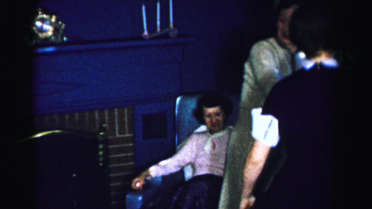 Woman in pink sweater sits in armchair beside a brick fireplace as another woman in a light dress stands nearby; Albany, New York, circa mid-1950s.