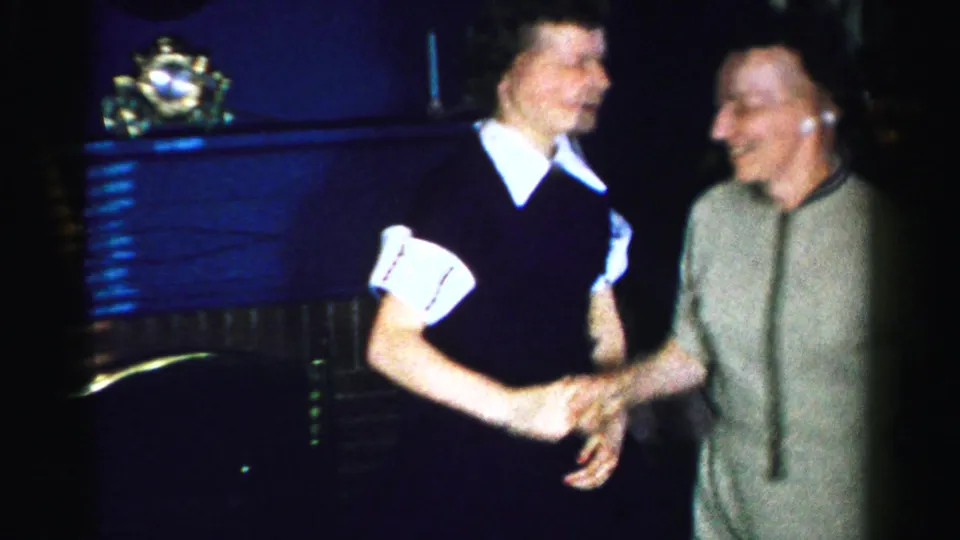 Two women clasp hands in a joyful dance pose; one in a dark dress with white collar, the other in a light gray dress; Albany, New York, circa mid-1950s.