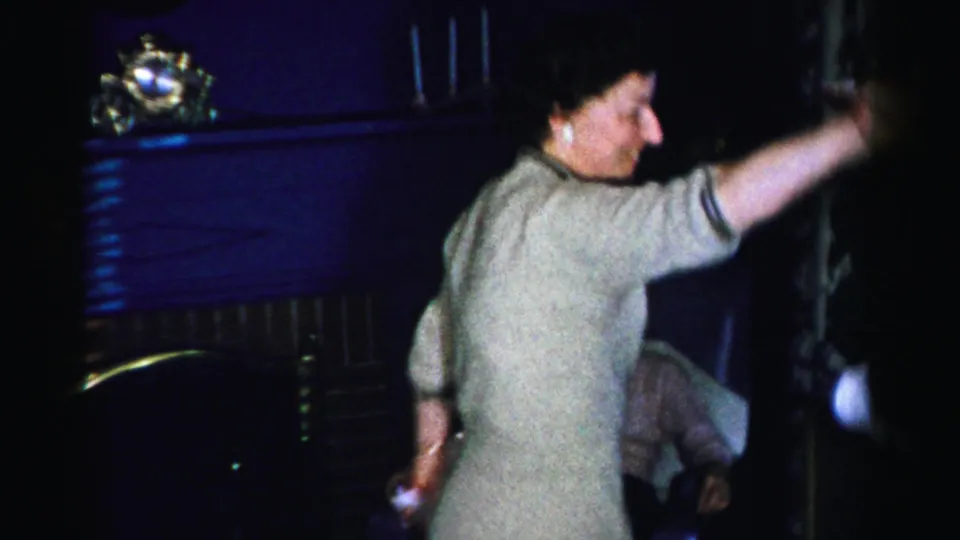 Woman in light gray dress extends her arm mid-dance beside a fireplace mantel with ornamental objects; mid-1950s home interior, Albany, New York.