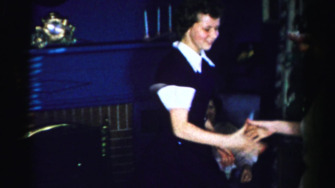 Close view of a smiling woman in a dark dress with white collar reaching out, likely mid-1950s Albany New York; additional figures are partially visible at the right frame edge.