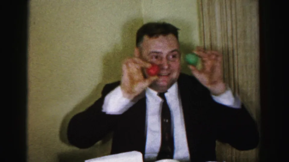 Grinning man in dark suit and narrow tie performs a comic gesture at a mid-1950s birthday party in Albany, New York, c. 1956.
