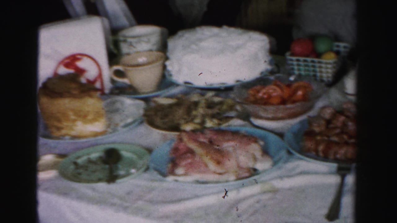 Mid-1950s Easter holiday table in Albany, New York, showing a white frosted cake, sliced ham, sausages, and dyed eggs in a checkered basket on a white linen cloth