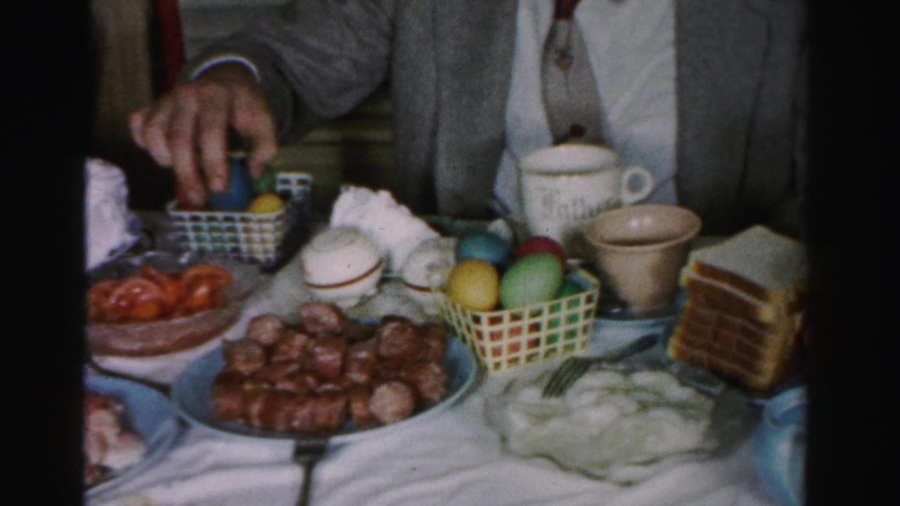 Late-1950s Easter holiday table, possibly Albany, New York — man in suit reaching for food; meatball platter, colored Easter egg basket, stacked toast and white mugs visible.