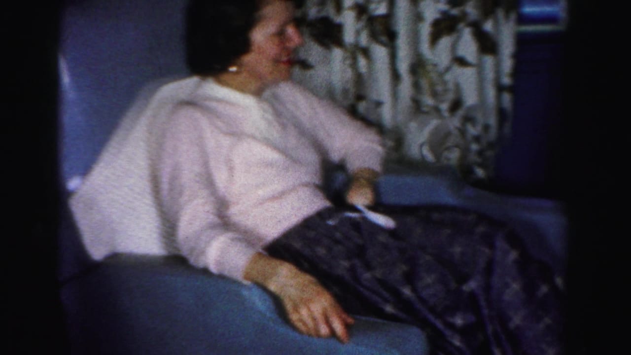 Woman seated in a blue armchair, turned toward the right side of the room.