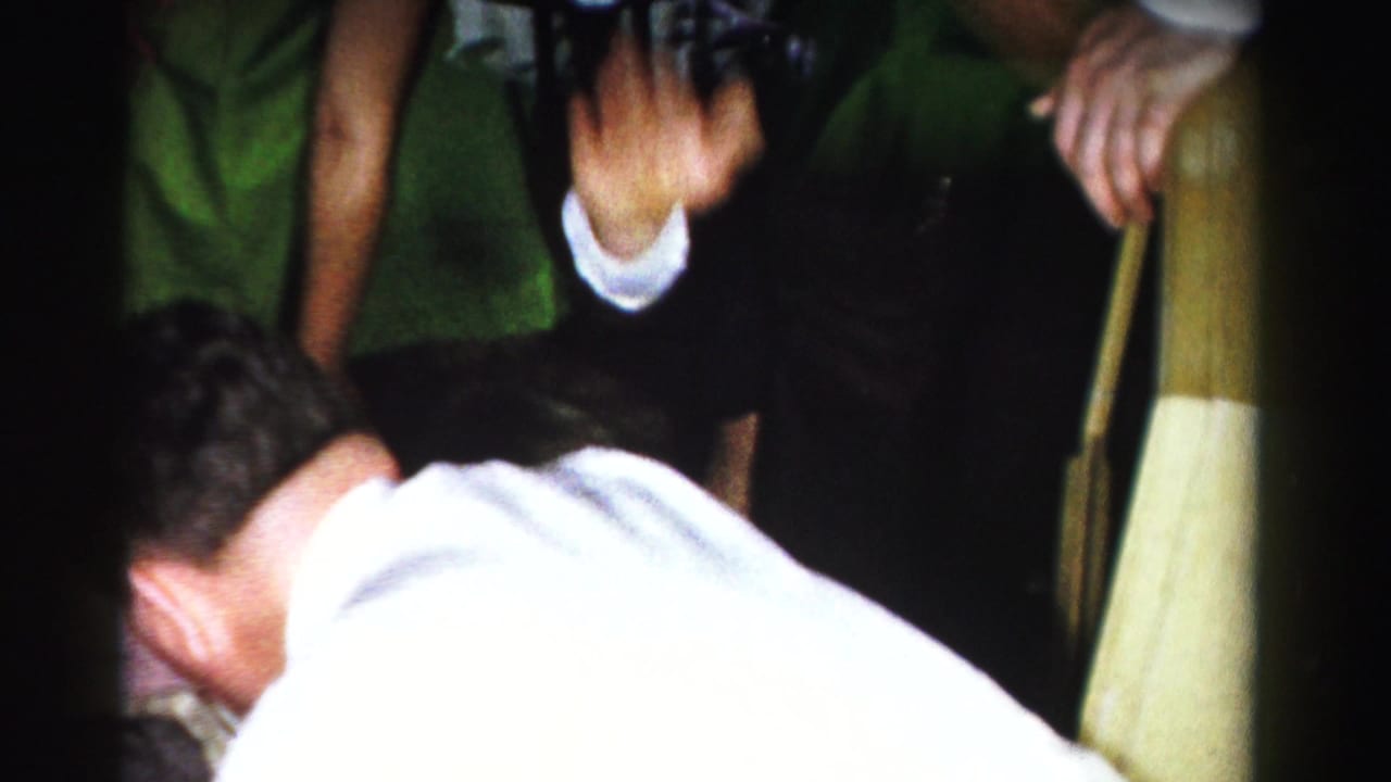 Person in white shirt bent sharply forward, green fabric visible in upper background, yellow-cream object at right edge of frame.