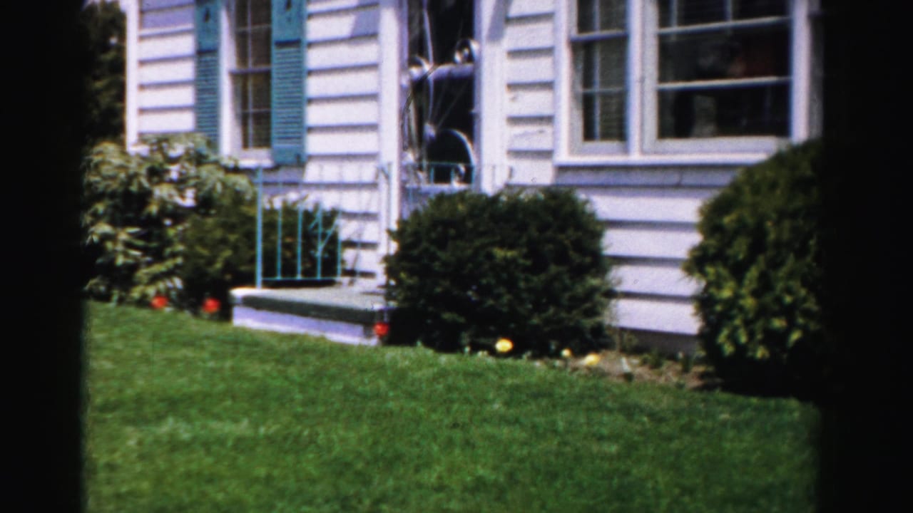 8mm color pan shot of white clapboard house with teal shutters, front steps with teal metal fence railing, and foundation shrubs, Albany NY area, mid-1950s.