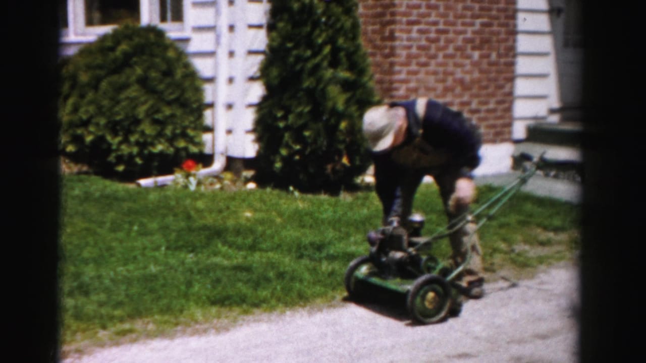 Man attempting to start a gasoline push mower in a suburban front yard, Albany, New York, circa mid-1950s, shot on 8mm color film.