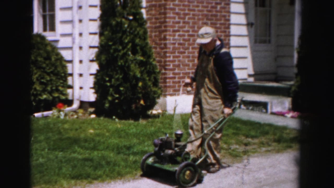 Man pausing beside a gasoline push mower in a tidy suburban front yard, Albany, New York, circa mid-1950s, 8mm home movie.
