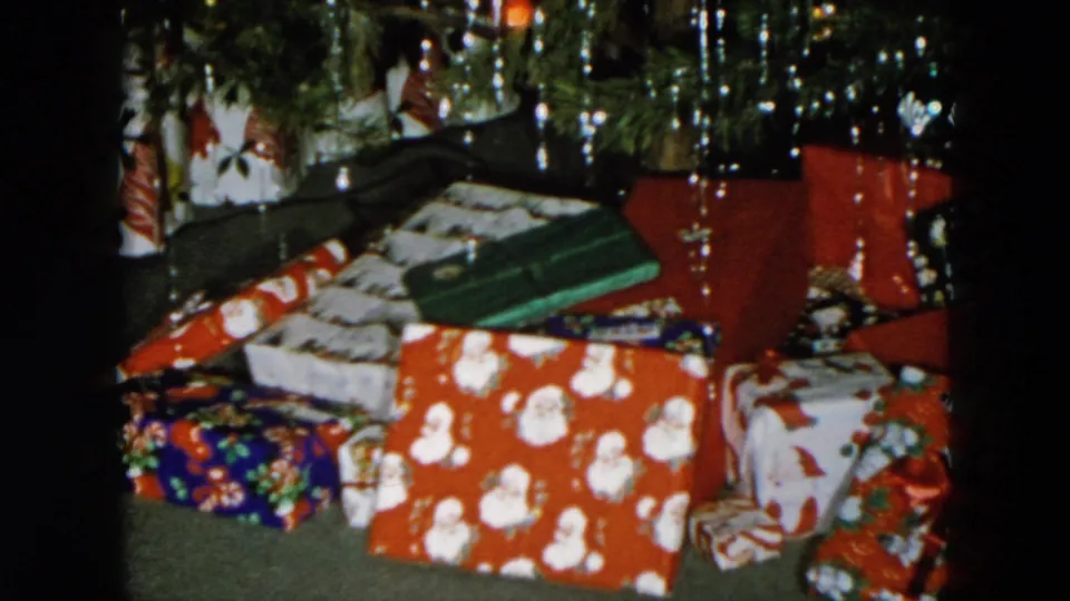 Static 8mm shot of holiday gifts under a tinsel-hung Christmas tree; Hicksville, New York, 1956.