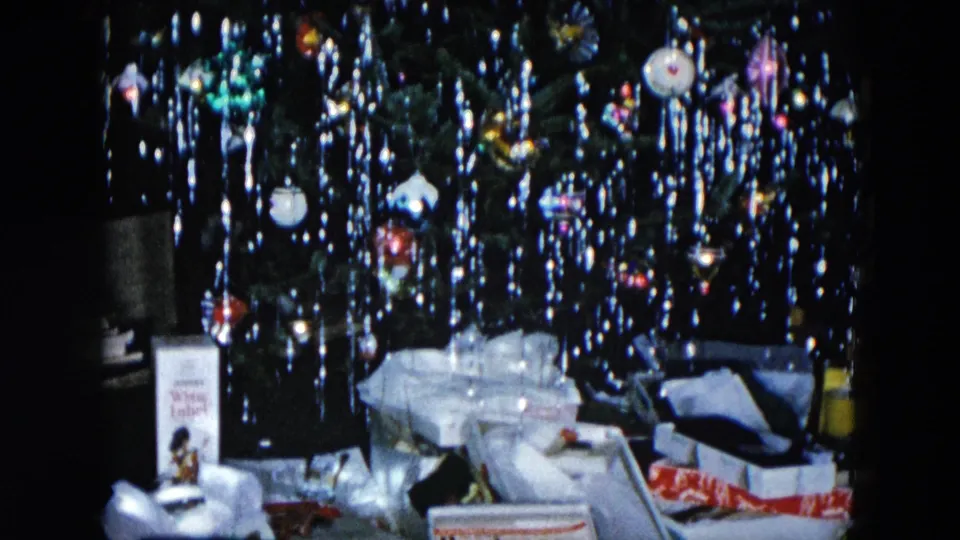 1956 Hicksville NY 8mm home movie: boxed gifts in foreground beneath cascading Christmas tree icicle tinsel and colored lights