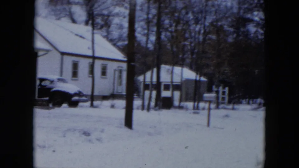 White house with snow-covered roof and a dark-colored 1950s sedan parked in the driveway, Hicksville, New York, circa 1956, on 8mm film.