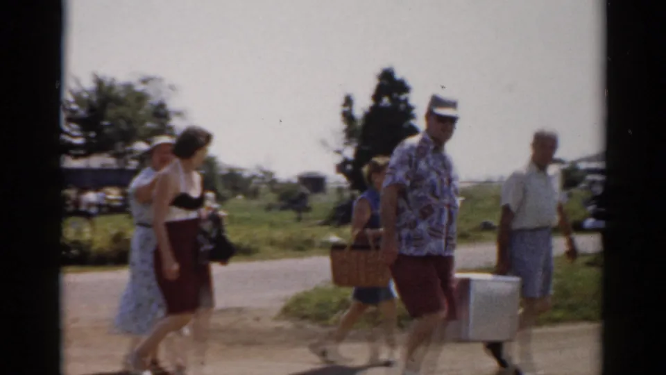 A woman, a man, and other adults continue past the camera with a cooler and picnic basket in 1957 Catskill, New York home-movie footage.