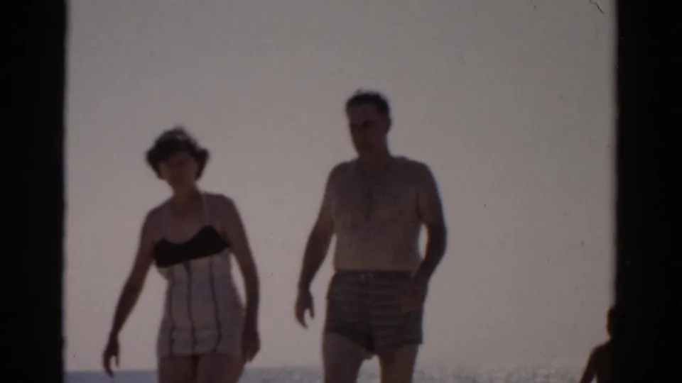 8mm film frame of a couple in late-1950s swimwear walking toward the camera on a beach; New York, circa 1957.
