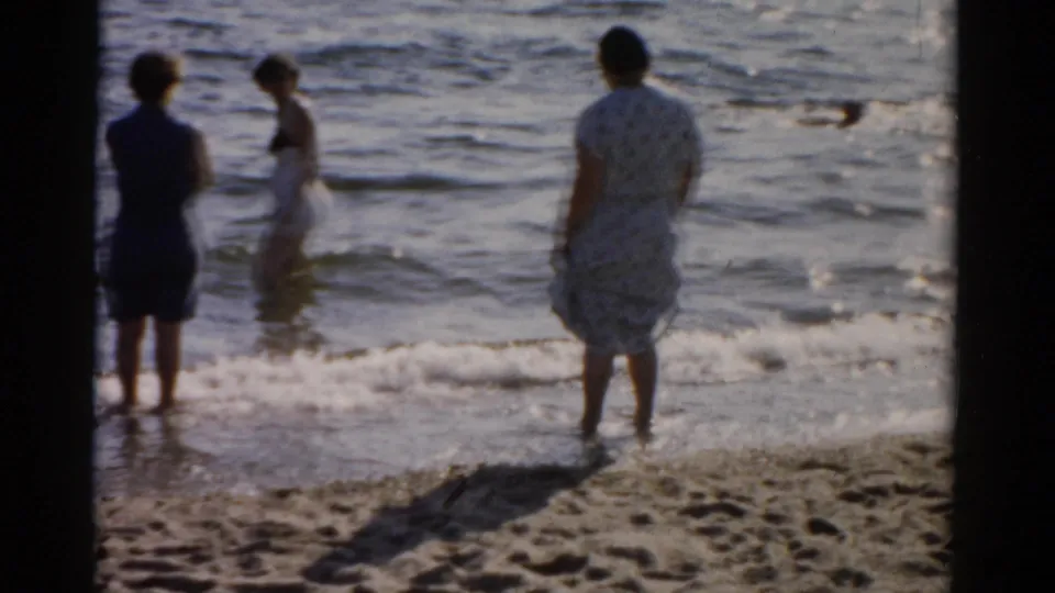 Women in mid-century summer dresses and swimwear stand at the waterline, facing outward, circa 1957, Catskill New York region.