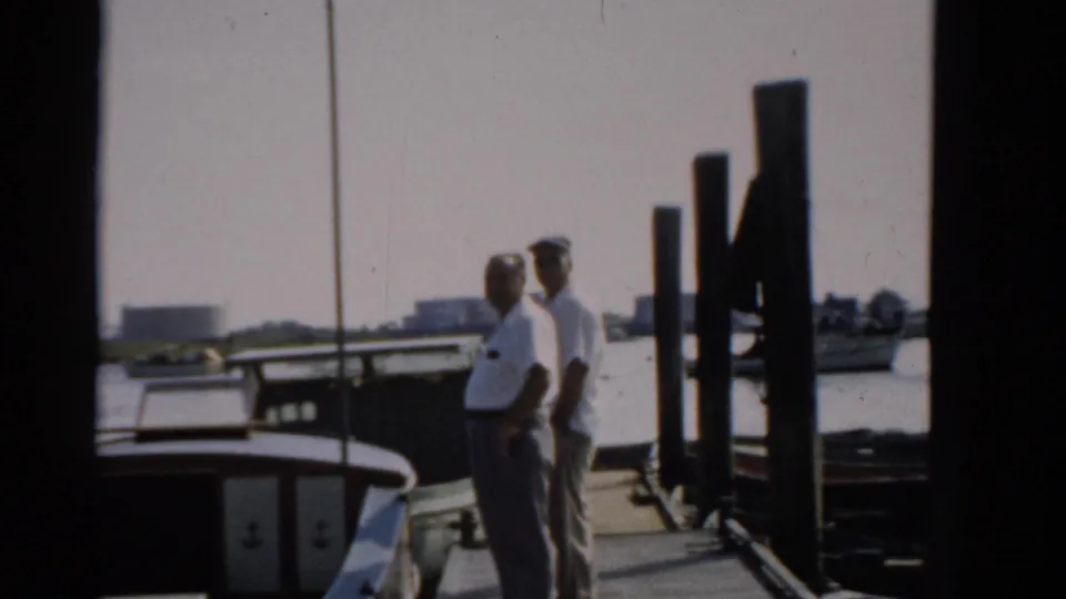 Two men in white shirts on a wooden dock near Catskill, New York, circa 1957, with waterfront structures visible in the background.