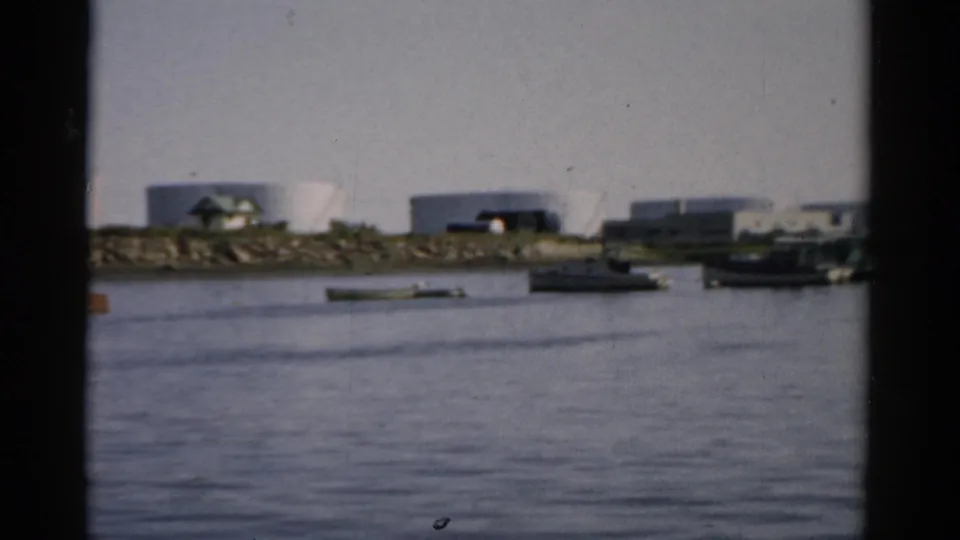 Catskill, New York waterway, c.1957 — moored boats with a red-orange element visible, white cylindrical storage tanks on far shore, 8mm home movie.