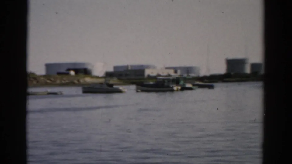 Catskill, New York waterway, c.1957 — cluster of small boats near industrial waterfront, multiple white storage tanks on far bank, 8mm home movie.