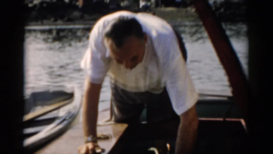Man in white short-sleeved shirt leans into a small wooden boat on calm water, a wristwatch visible on his wrist, Catskill, New York, c. 1957.