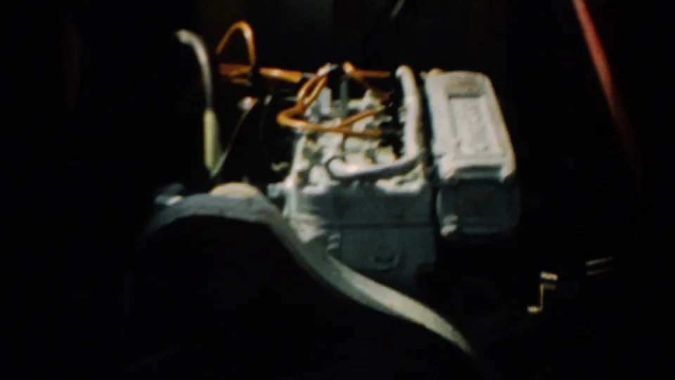 A mid-century boat motor with orange wiring filmed at close range on 8mm in dim light, circa 1957.