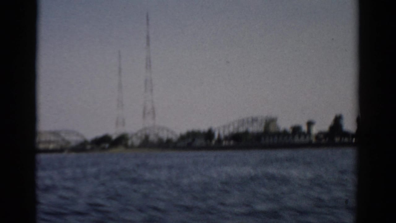Mid-clip 8mm frame c.1957, Catskill-area lake, showing roller coaster track and broadcast towers on the far shore as the boat continues.