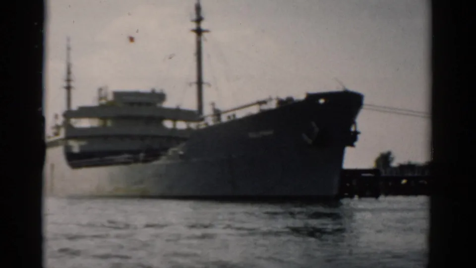 Large dark-hulled cargo freighter passing on calm water, shot on 8mm film circa 1957, possibly the Hudson River near Catskill, New York.