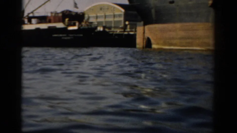 Barge or cargo vessel at dock, Catskill NY waterfront, c. 1957 — curved-roof shore building behind hull on 8mm color film.