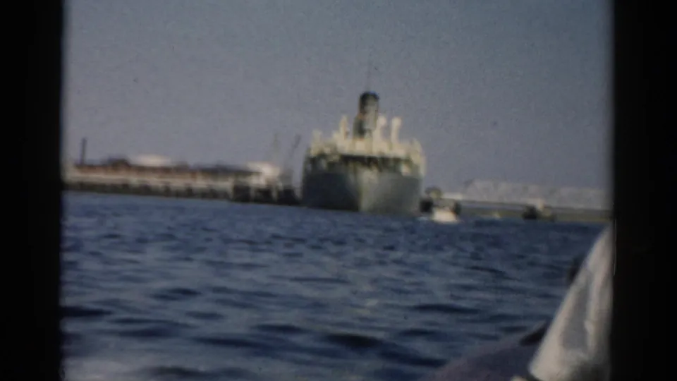 Wide view of a large passenger vessel at a harbour pier, seen from a moving small boat, ca. 1957 New York.