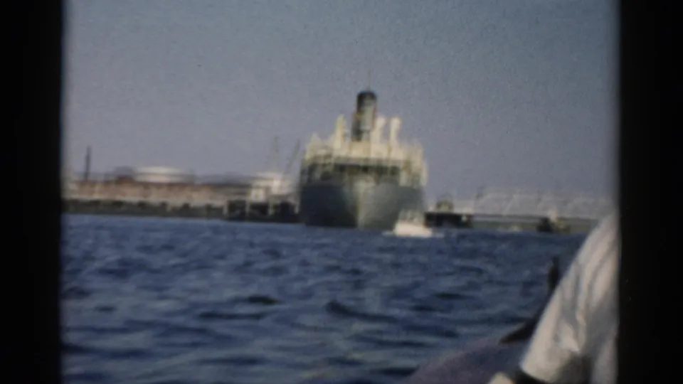 Passenger vessel at harbour pier on closer approach, ca. 1957; person in boat visible at lower right corner of frame.