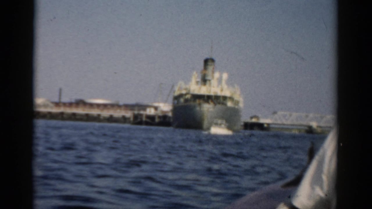 Large mid-century cargo or passenger ship docked at a pier, filmed from a small boat on choppy water, circa 1957, Catskill New York area.